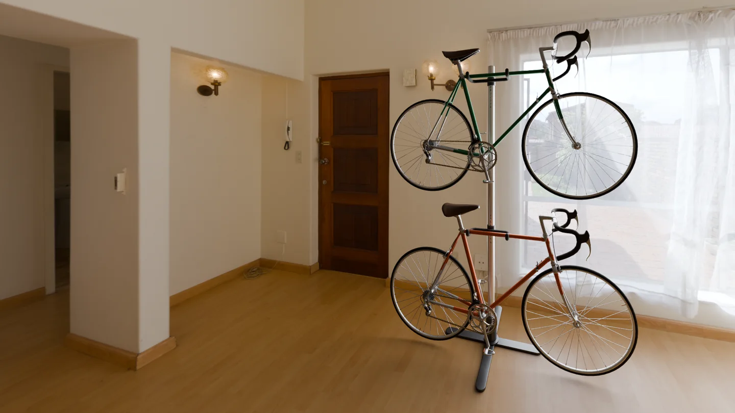 A silver Duo rack holds green and clay bicycles beside the entrance door, with its crossed base resting on the oak floor